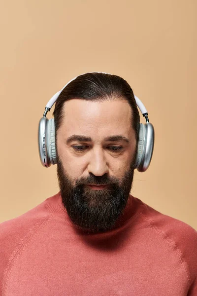 Bel homme barbu en pull à col roulé rose écoutant de la musique dans des écouteurs sans fil sur beige — Photo de stock