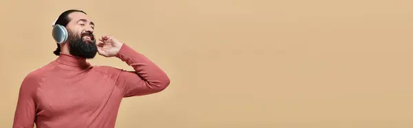 Smiling bearded man in turtleneck jumper listening music in wireless headphones, happy person banner — Stock Photo