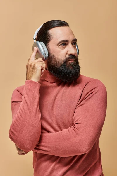 Bonito barbudo homem em gola alta jumper ouvir música em fones de ouvido sem fio no fundo bege — Fotografia de Stock