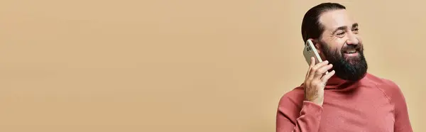 Banner of cheerful bearded man in turtleneck jumper talking on smartphone on beige background — Stock Photo