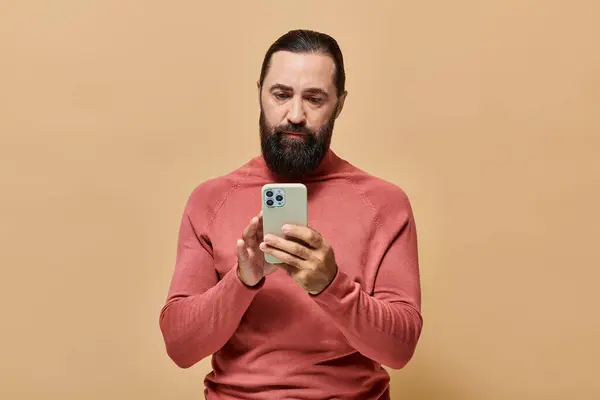 Portrait d'un bel homme barbu en pull à col roulé utilisant un smartphone sur fond beige — Photo de stock