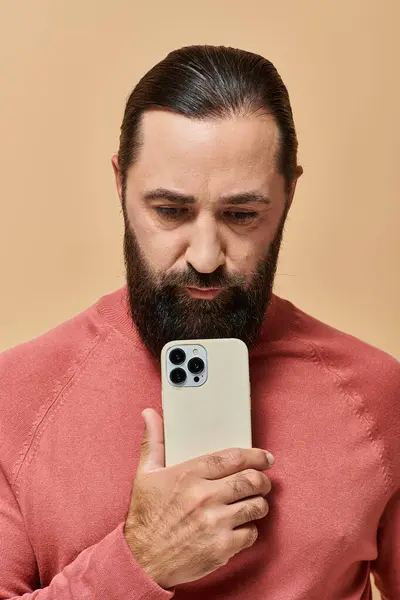 Портрет хорошого виглядає бородатого чоловіка в стрибку з водоростями, фотографуючи на смартфоні, бежевий фон — стокове фото