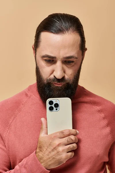 Portrait of good looking bearded man in turtleneck jumper taking photo on smartphone, beige backdrop — Stock Photo