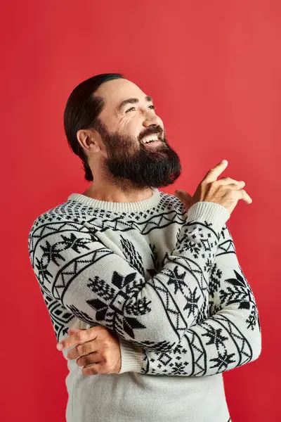 Щасливий бородатий чоловік в зимовому светрі з орнаментом, посміхаючись на червоному тлі, з Різдвом — стокове фото