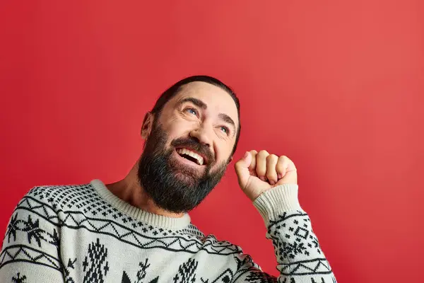 Весёлый бородатый мужчина в зимнем свитере с орнаментом, стучащий в красный фон, Счастливого Рождества — стоковое фото