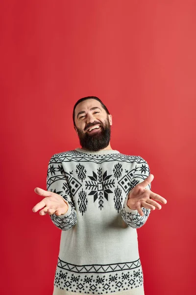 Happy bearded man in winter sweater with ornament gesturing on red backdrop, Merry Christmas — Stock Photo