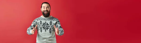 Happy bearded man in Christmas sweater with ornament gesturing on red, winter holidays banner — Stock Photo