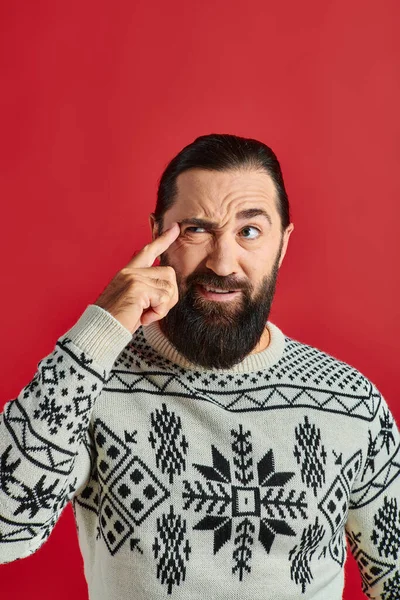 Бородатый мужчина в рождественском свитере с орнаментом мышления и указывая на голову на красном фоне — стоковое фото