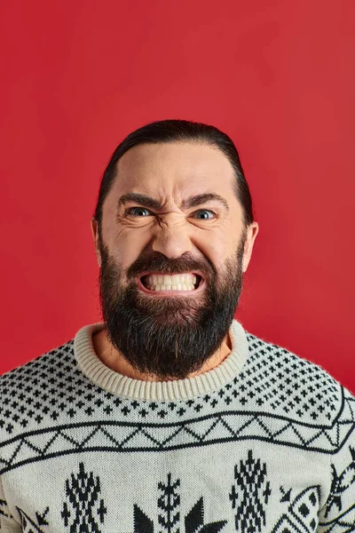 Bearded man in winter sweater with ornament grinning on red backdrop, Christmas and New Year — Stock Photo