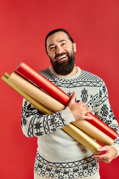Heureux homme barbu en pull de Noël tenant papier d'emballage sur fond rouge, les ventes de vacances — Photo de stock
