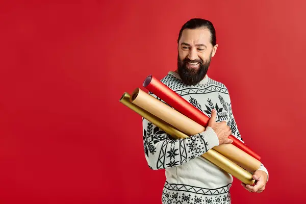 Heureux homme barbu en pull de Noël tenant papier d'emballage sur fond rouge, les ventes de vacances — Photo de stock