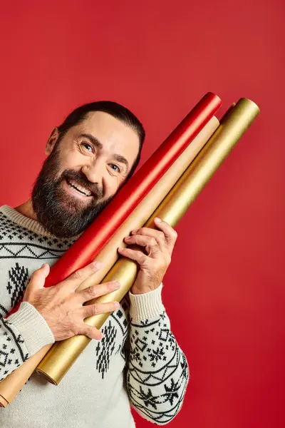 Hombre barbudo feliz en suéter de invierno sosteniendo papel de embalaje sobre fondo rojo, Feliz Navidad - foto de stock