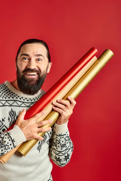 Fröhlicher bärtiger Mann im Winterpullover mit Geschenkpapier auf rotem Hintergrund, Frohe Weihnachten — Stockfoto