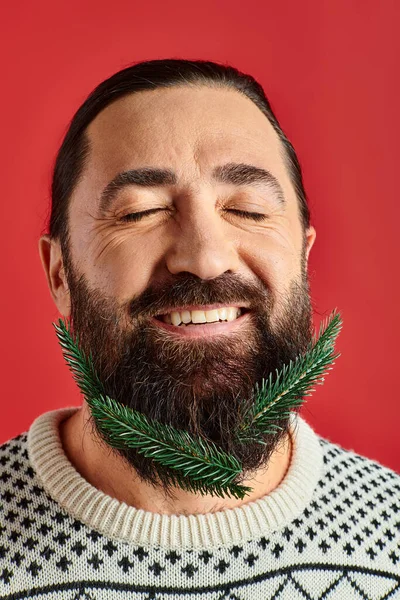 Happy man in winter sweater holding branches with fresh spruce on red backdrop, Merry Christmas — Stock Photo