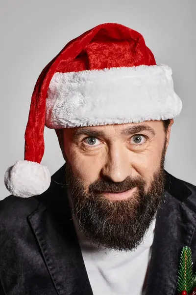 Retrato de hombre guapo barbudo en traje elegante y sombrero de santa posando sobre fondo gris, Navidad - foto de stock