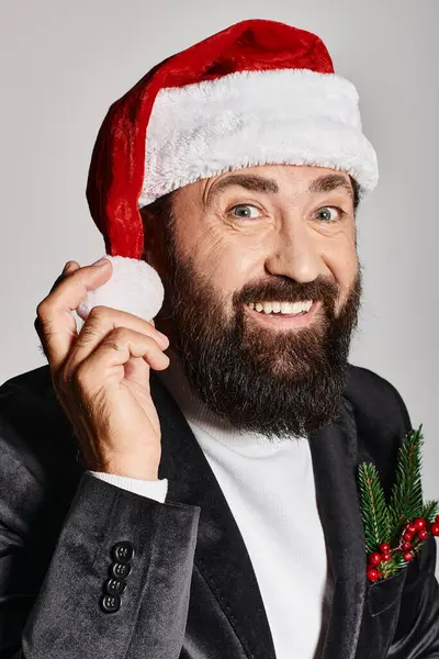 Retrato de hombre guapo positivo en traje elegante y sombrero de santa posando sobre fondo gris, Navidad - foto de stock