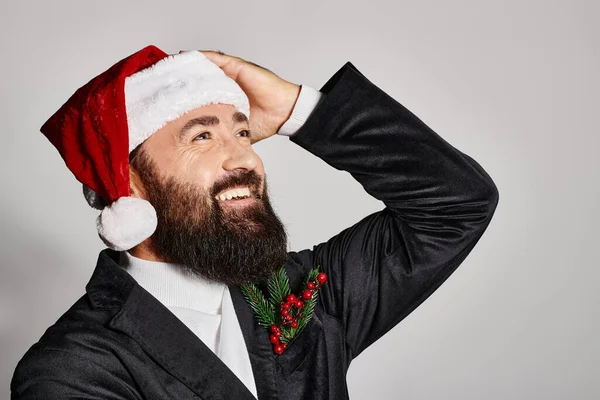 Retrato de homem bonito barbudo em terno elegante e chapéu de Papai Noel sorrindo no fundo cinza, Natal — Fotografia de Stock