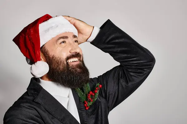 Portrait of bearded handsome man in elegant suit and santa hat smiling on grey backdrop, Christmas — Stock Photo