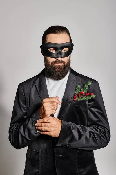 Рождественский бал-маскарад, красивый бородатый мужчина в карнавальной маске и элегантный костюм на сером фоне — стоковое фото