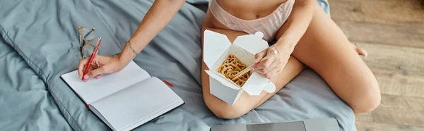 Vista recortada de la mujer sexy sentada en la cama y tomando notas mientras trabaja desde casa, pancarta - foto de stock