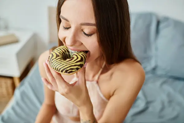 Giovane donna attraente in lingerie sexy mangiare deliziosa ciambella con gli occhi chiusi a casa sua — Foto stock