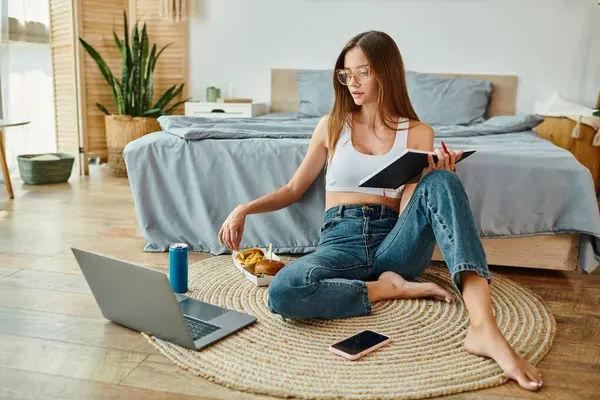 Thoughtful young woman in casual attire sitting on floor with her notes and working on laptop — Stock Photo