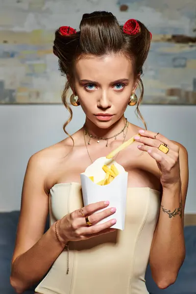 Atraente mulher sexy com feno rolos em espartilho bege segurando pacote de batatas fritas e olhando para a câmera — Fotografia de Stock