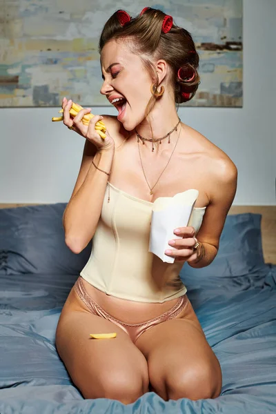 Mujer hermosa emocional en corsé sexy beige con accesorios posando en movimiento con papas fritas en las manos - foto de stock