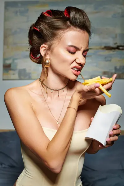 Mulher atraente emocional em espartilho sexy com acessórios e encrespadores de cabelo posando com batatas fritas — Fotografia de Stock
