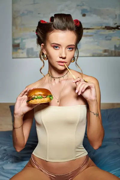 Appealing sexy woman in beige alluring corset holding delicious burger and looking at camera — Stock Photo