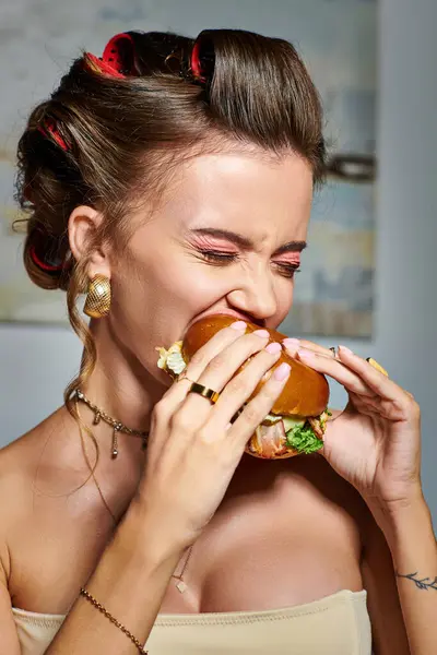 Alluring young beautiful women with accessories and tattoo on hand eating huge delicious burger — Stock Photo