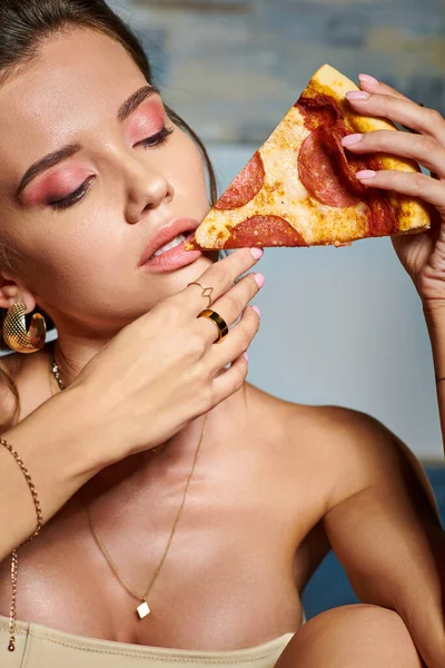 Joven hermosa mujer con accesorios en beige sexy corsé listo para comer rebanada de deliciosa pizza - foto de stock