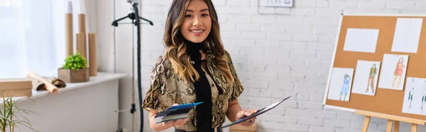 Happy asian fashion designer with color samples looking at camera in own studio, horizontal banner — Stock Photo