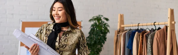 Joyeux concepteur de vêtements asiatiques tenant des motifs de couture dans son propre atelier, entreprise de mode, bannière — Photo de stock