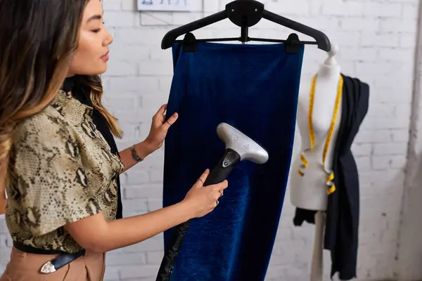 Jovem estilista asiático elegante fumegante tecido de veludo macio em atelier roupas sob medida, negócios de moda — Fotografia de Stock