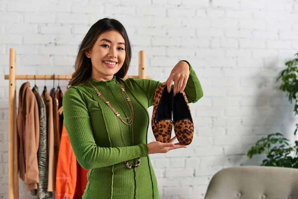 Overjoyed asiático estilista pessoal mostrando moda animal imprimir sapatos no próprio atelier, negócios de moda — Fotografia de Stock
