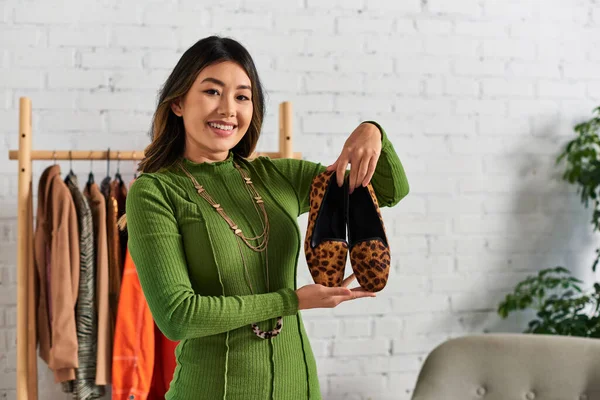 Overjoyed asian personal stylist showing trendy animal print shoes in own atelier, fashion business — Stock Photo