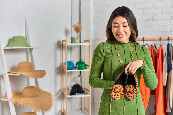 Улыбающийся азиатский дизайнер одежды, показывающий стильные туфли для печати животных в частных ателье, малый бизнес — стоковое фото