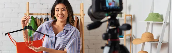 Heureux asiatique designer montrant crop top et accessoires pendant vlog mode dans atelier privé, bannière — Photo de stock