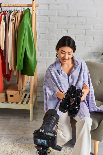 Щасливий азіатський особистий стиліст, що демонструє модні босоніжки під час відеоблогу в приватній моді ательє — стокове фото