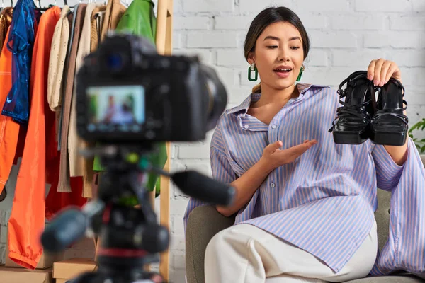 Attractive asian clothes designer showing stylish footwear during fashion vlog in private studio — Stock Photo