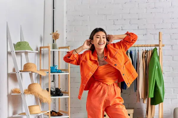 Overjoyed asiático designer de roupas em laranja brilhante casual traje olhando para a câmera no próprio estúdio — Fotografia de Stock