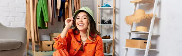 Joyeuse styliste asiatique posant en tenue orange et chapeau panama en atelier, entreprise de mode, bannière — Photo de stock