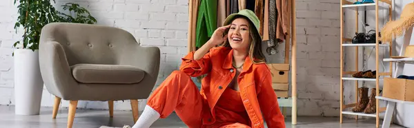 Sonriente asiático diseñador en naranja atuendo y panama sombrero sonriendo a cámara en privado atelier, bandera - foto de stock