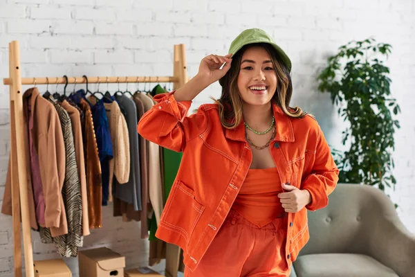 Креативний азіатський дизайнер в помаранчевому одязі та панамському капелюсі в сучасному ательє моди, малий бізнес — стокове фото