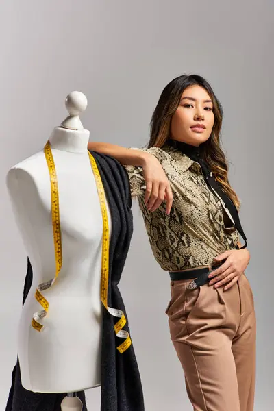 Молодий привабливий азіатський дизайнер, дивлячись на камеру біля манікюру з тканиною і мірною стрічкою — стокове фото