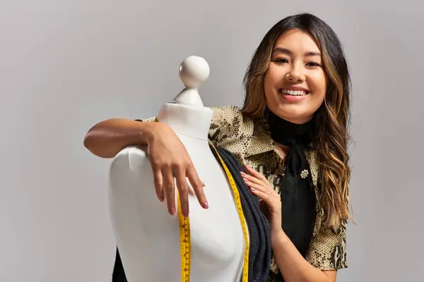 Entzückte asiatische Kleidungsdesignerin blickt mit Maßband auf graue Schaufensterpuppe — Stockfoto