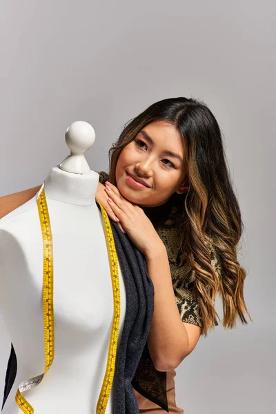 Мрійливий азіатський дизайнер одягу, дивлячись далеко від манікюру з мірною стрічкою на сірому тлі — стокове фото