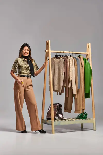 Alegre asiático designer com fita métrica perto rack com roupas na moda no fundo cinza — Fotografia de Stock