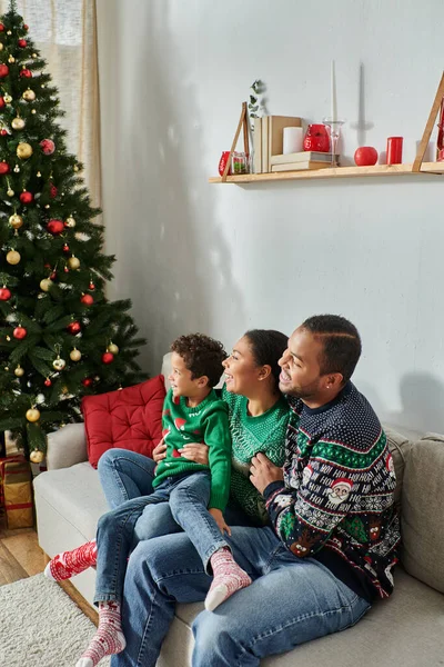 Plano vertical de la familia afroamericana sentada junto al árbol de Navidad y sonriendo alegremente - foto de stock